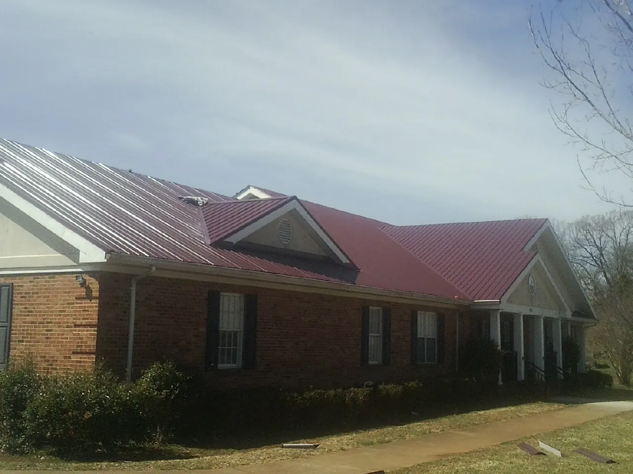 Red metal roof with gabled entries on a long brick building, from a Hail Damage Roof Repair job in Kent